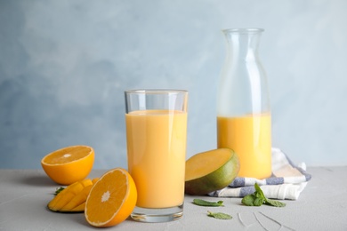 Fresh mango drink and tropical fruits on table against color background