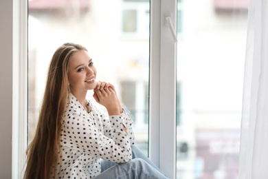 Beautiful young woman on windowsill at home