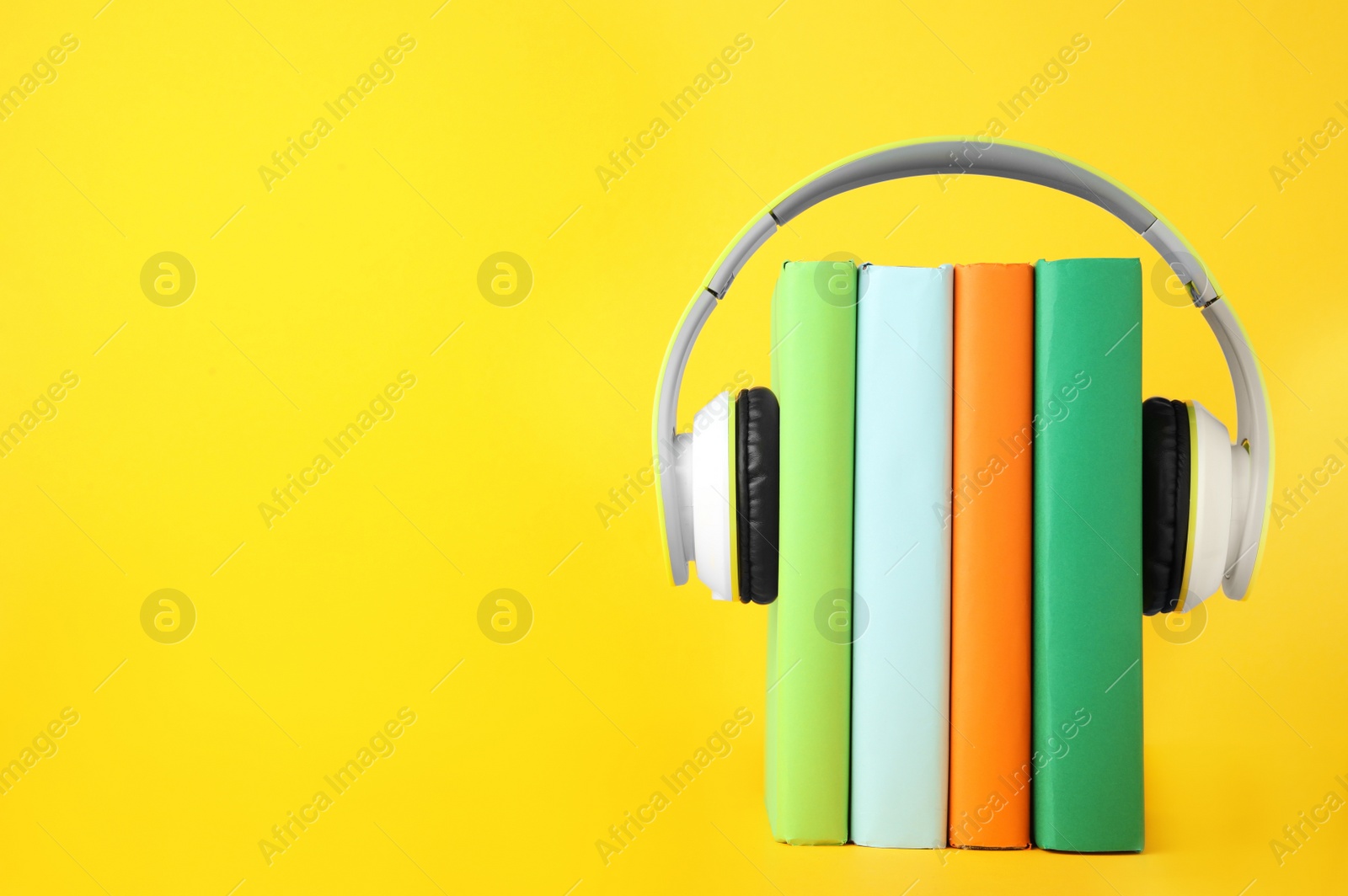 Photo of Books with modern headphones on yellow background. Space for text