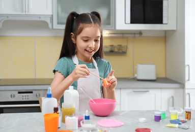 Photo of Cute little girl making homemade slime toy at table in kitchen