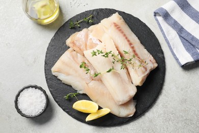 Photo of Pieces of raw cod fish, lemon, salt and oil on light grey table, top view