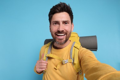 Photo of Happy man with backpack taking selfie on light blue background. Active tourism