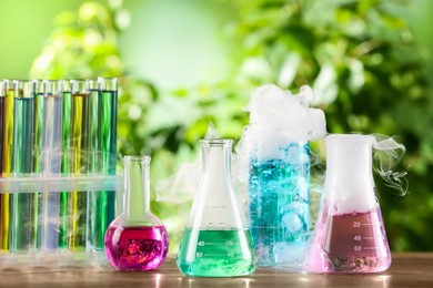 Laboratory glassware and test tubes with colorful liquids on wooden table outdoors. Chemical reaction