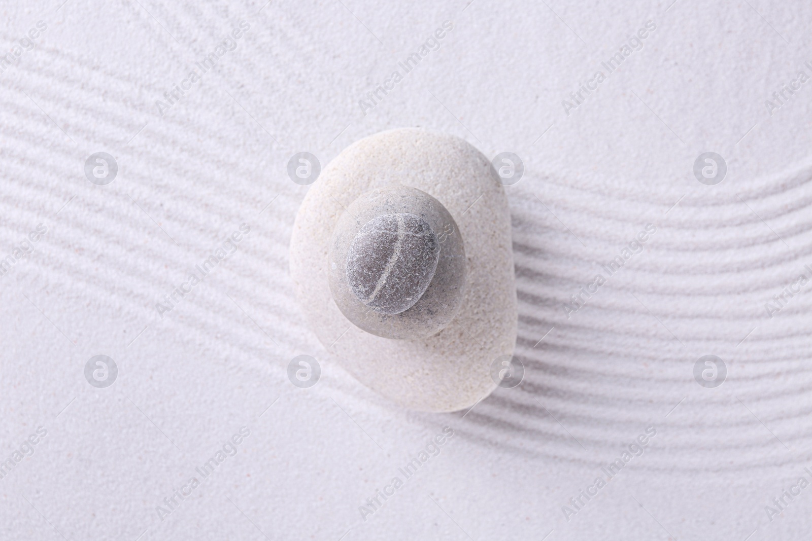 Photo of Zen garden stones on white sand with pattern, top view