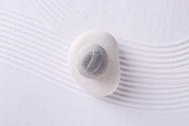 Photo of Zen garden stones on white sand with pattern, top view