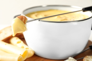 Photo of Pot of delicious cheese fondue and fork with bread on table