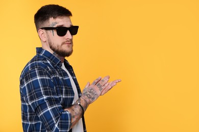 Photo of Handsome hipster man wearing stylish sunglasses on yellow background. Space for text