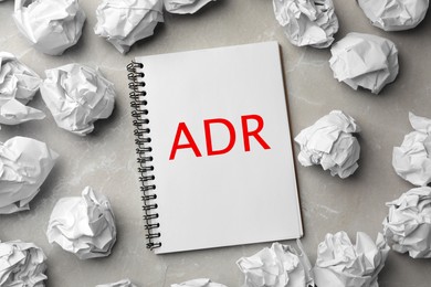 Image of Alternative dispute resolution. Notebook with abbreviation ADR surrounded by paper balls on light grey table, flat lay
