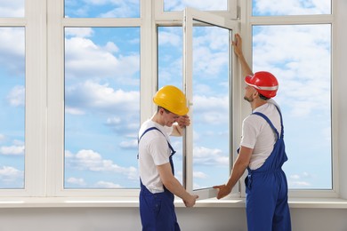 Photo of Workers in uniform installing plastic window indoors