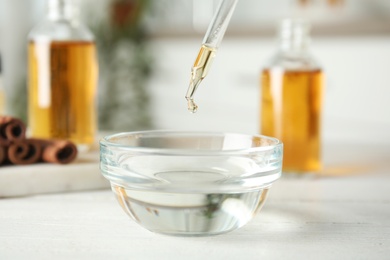 Photo of Pipette with cinnamon essential oil over bowl of water on table