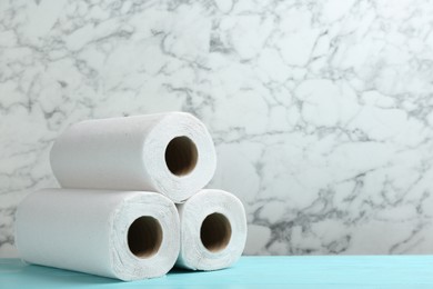 Photo of Rolls of paper towels on turquoise wooden table against marble wall, space for text