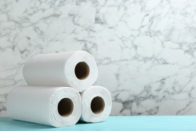 Rolls of paper towels on turquoise wooden table against marble wall, space for text