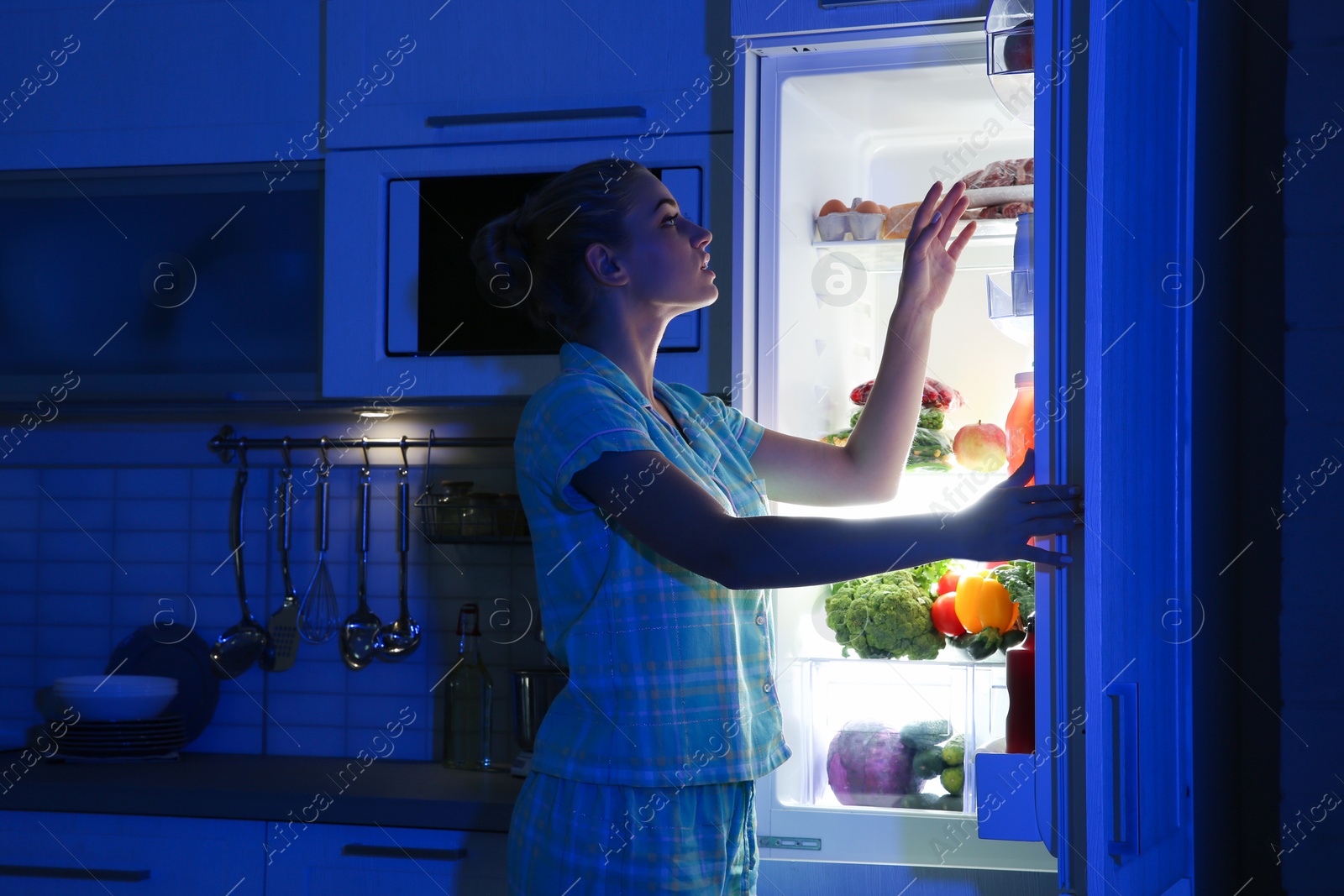 Photo of Woman choosing food from refrigerator in kitchen at night