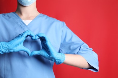 Photo of Doctor making heart with hands on red background, closeup