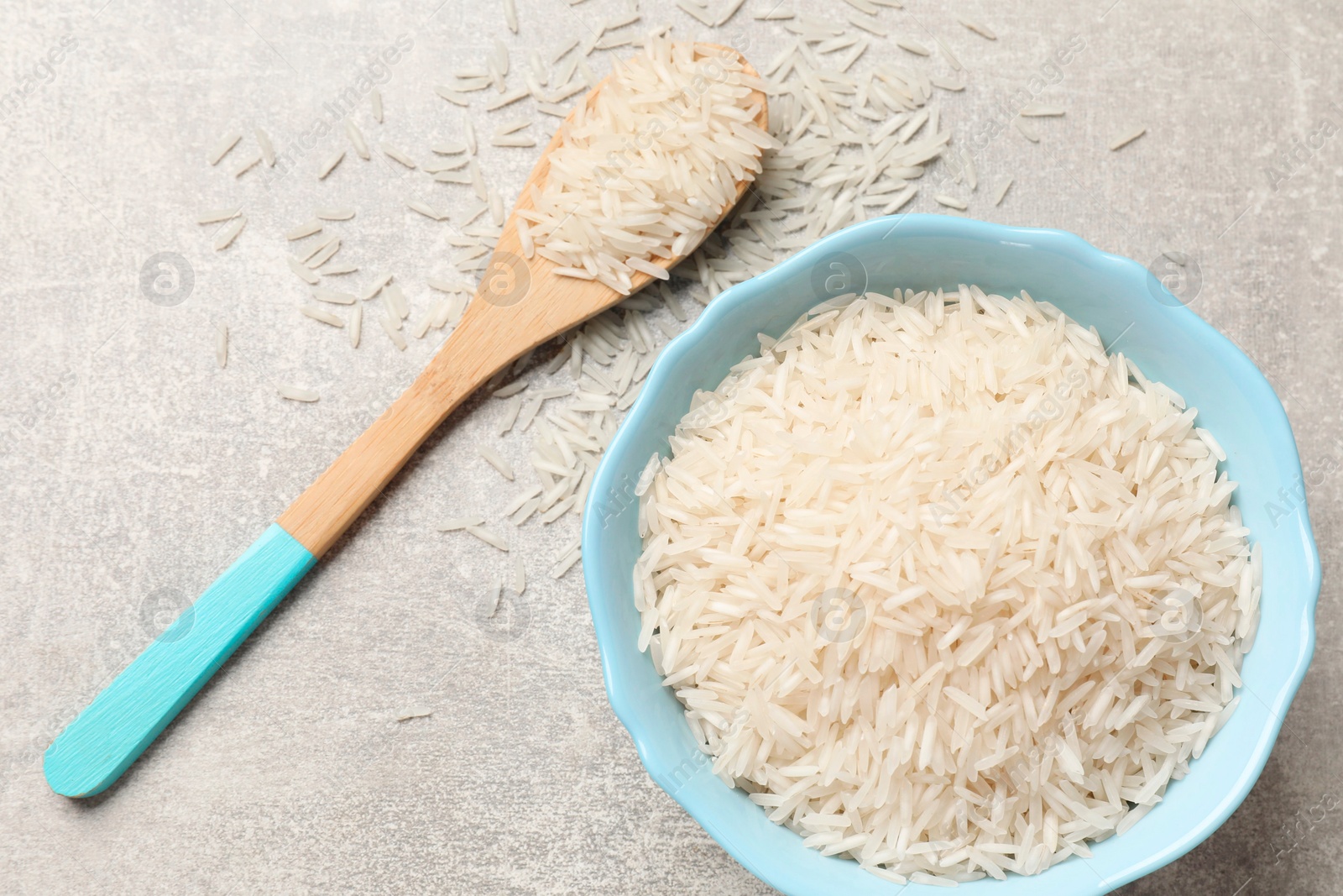 Photo of Raw basmati rice in bowl and spoon on grey table, top view