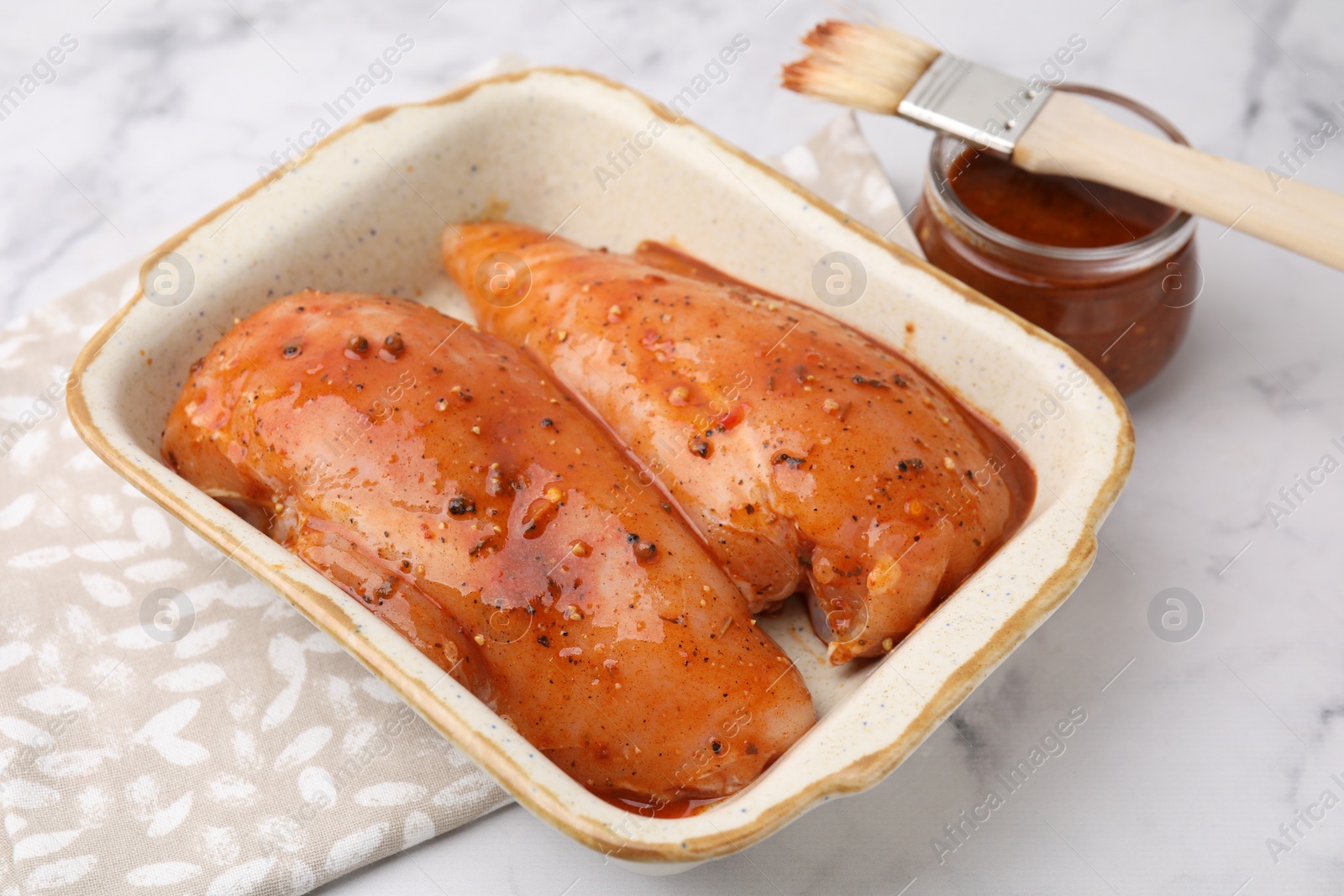 Photo of Raw marinated chicken fillets on white marble table