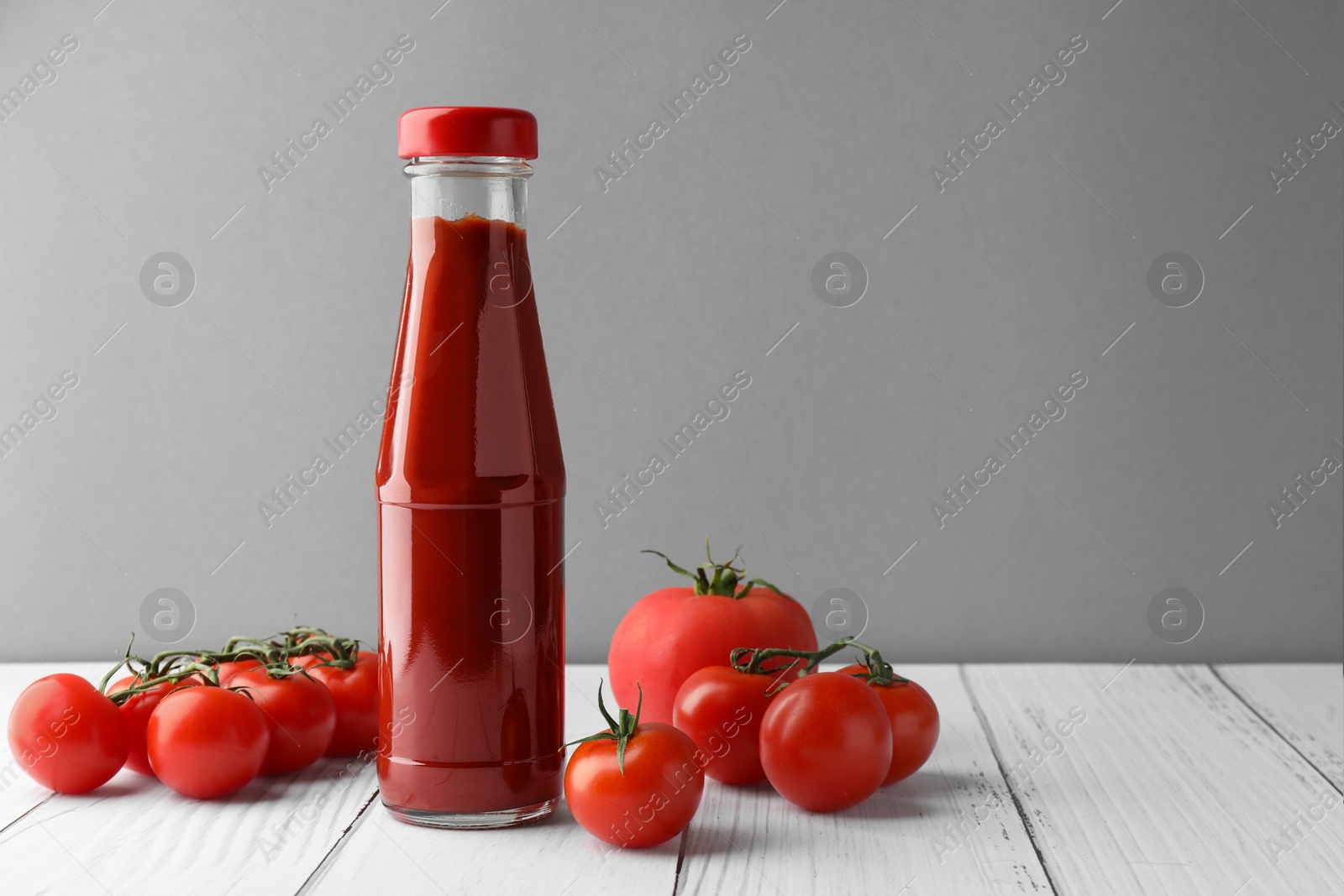 Photo of Bottle of tasty ketchup and tomatoes on white wooden table. Space for text