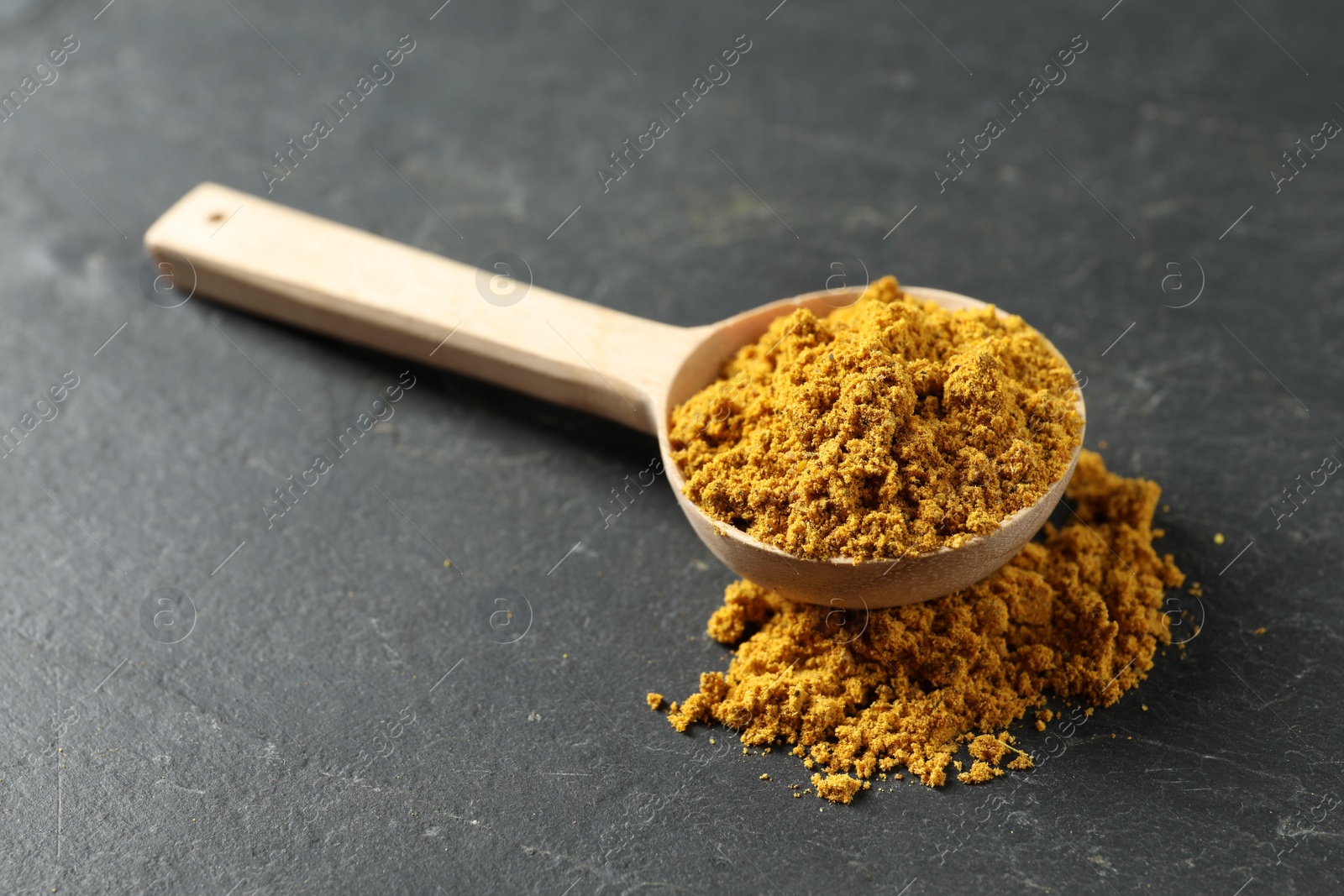 Photo of Spoon with dry curry powder on dark textured table, closeup