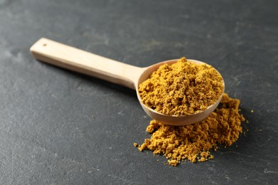 Spoon with dry curry powder on dark textured table, closeup