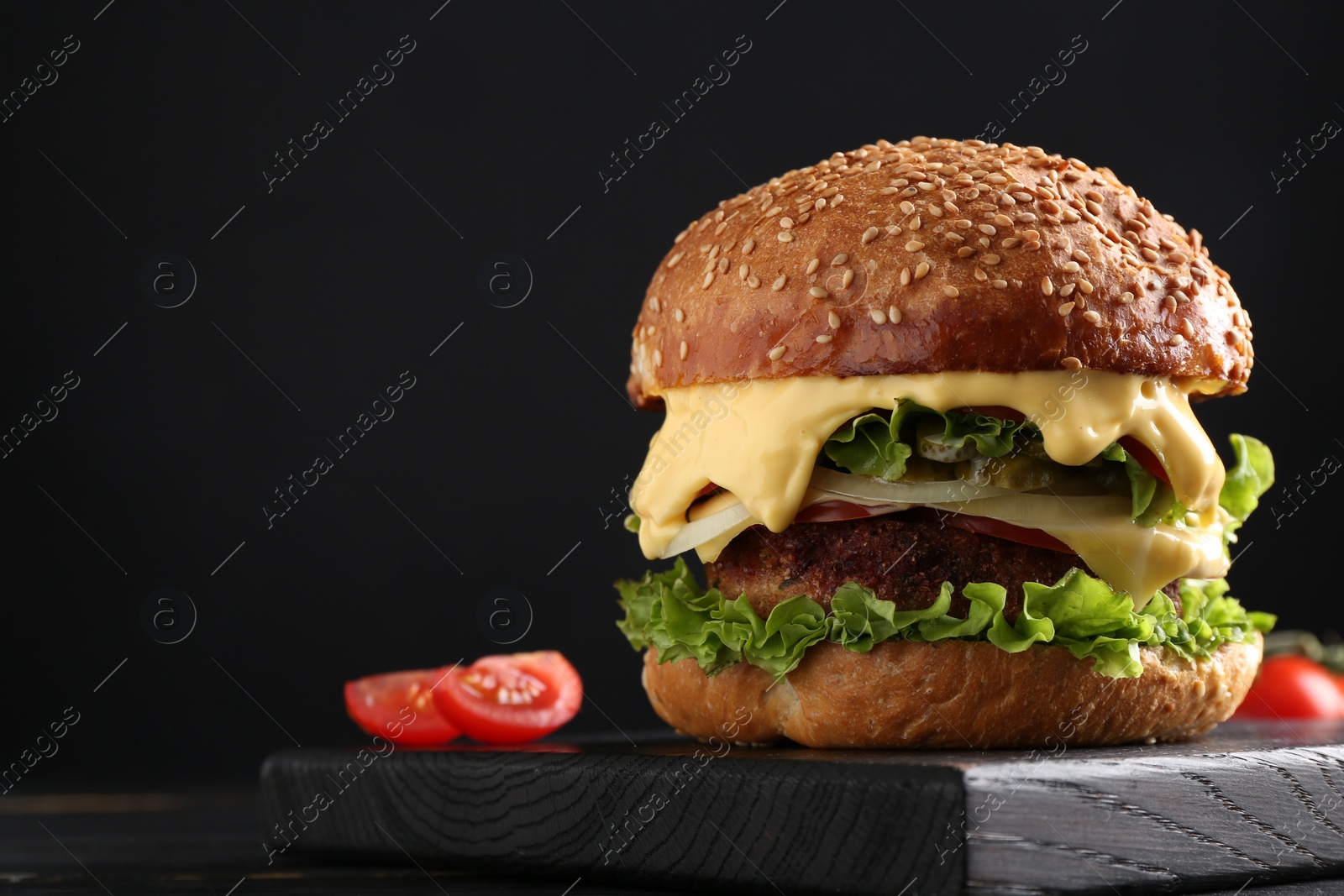 Photo of Vegetarian burger with delicious patty on black wooden table, closeup. Space for text