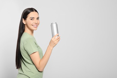 Beautiful happy woman holding beverage can on light grey background. Space for text