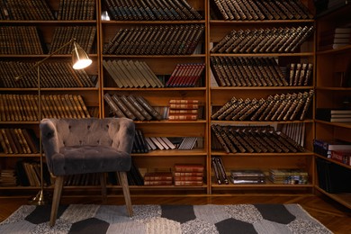 Photo of Cozy home library interior with comfortable armchair and collection of vintage books on shelves
