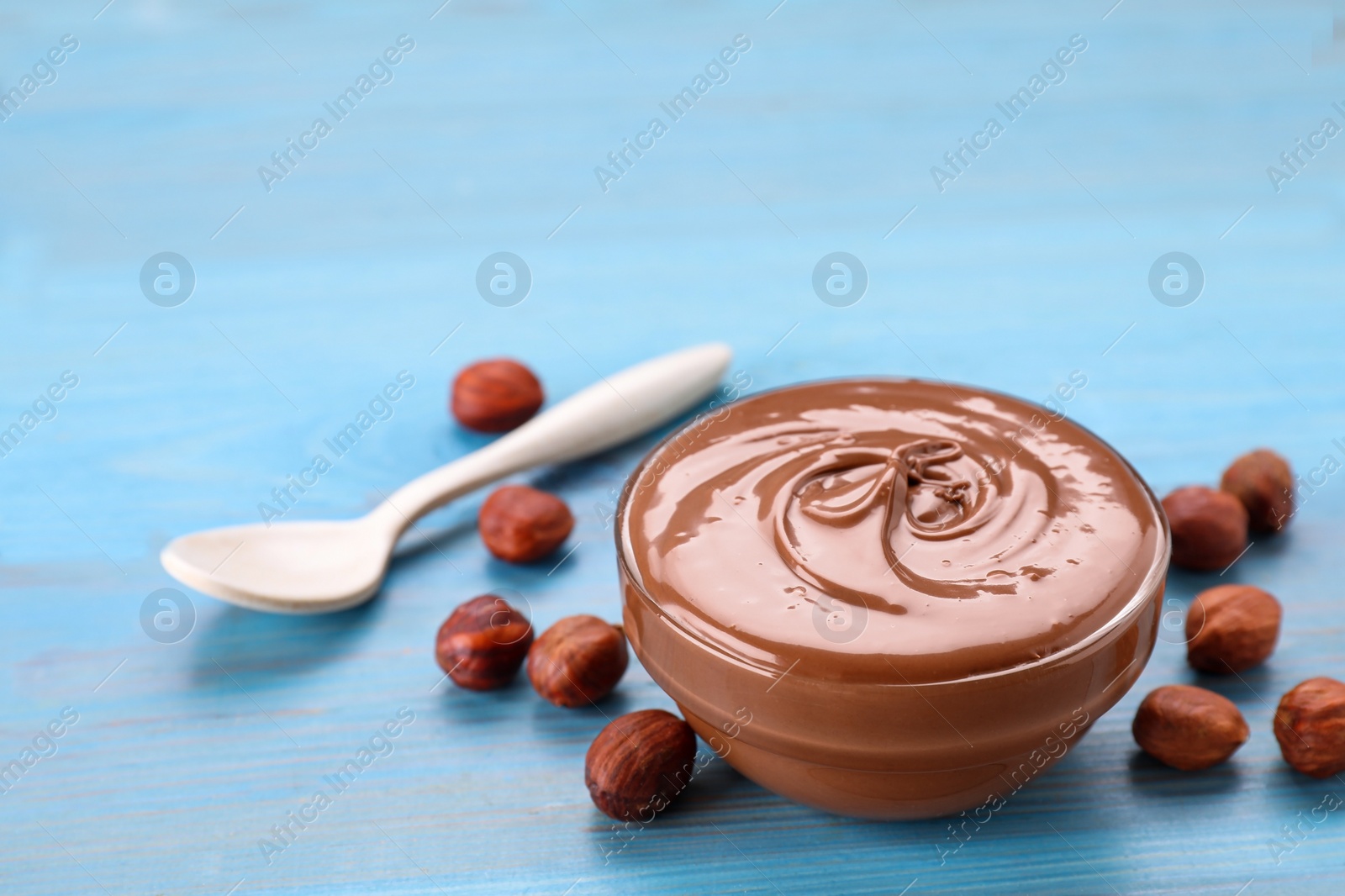 Photo of Bowl with tasty chocolate paste and nuts on light blue wooden table