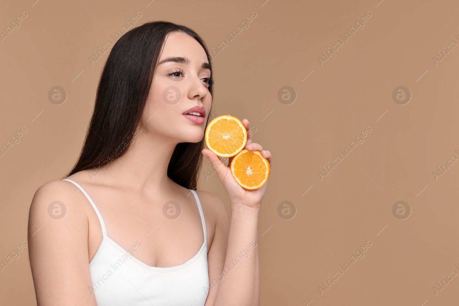 Photo of Beautiful young woman with pieces of orange on beige background. Space for text