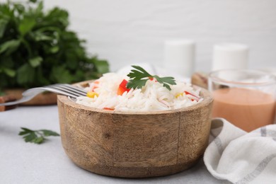 Photo of Bowl of delicious rice with vegetables and parsley served on light gray table, closeup