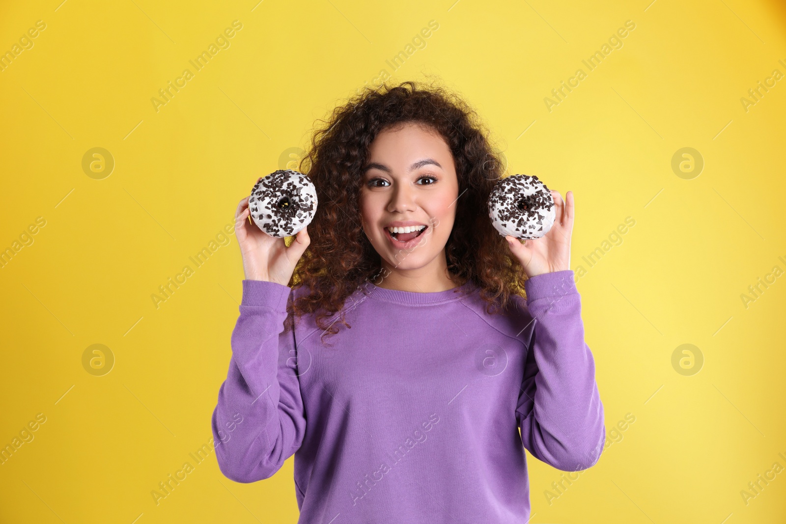 Photo of Beautiful African-American woman with donuts on yellow background