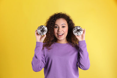 Beautiful African-American woman with donuts on yellow background