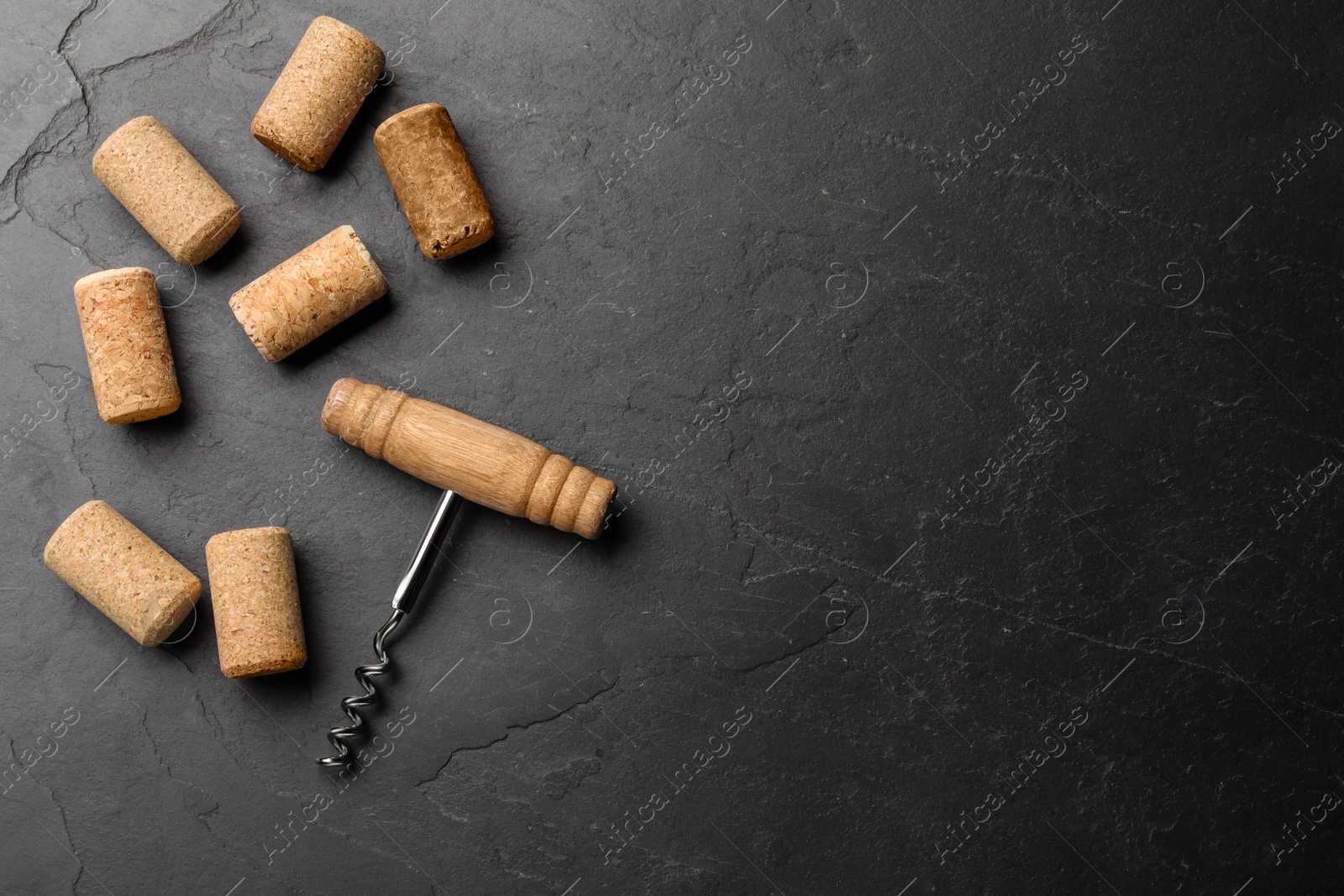 Photo of Corkscrew and wine bottle stoppers on slate table, flat lay. Space for text