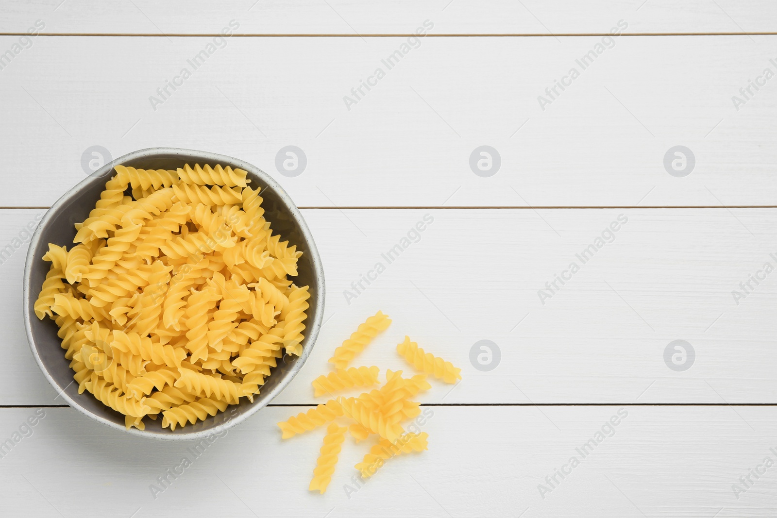 Photo of Raw fusilli pasta in bowl on white wooden table, top view. Space for text