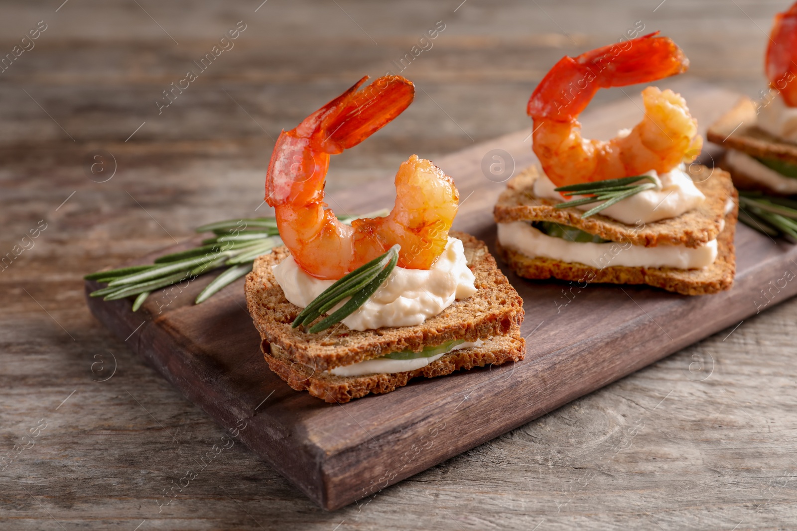 Photo of Delicious small sandwiches with shrimps on wooden board