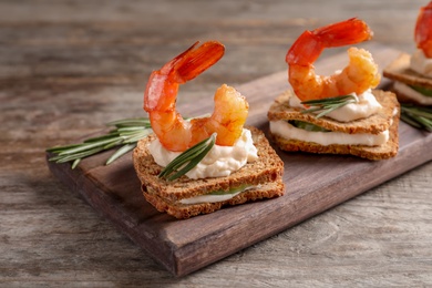 Photo of Delicious small sandwiches with shrimps on wooden board