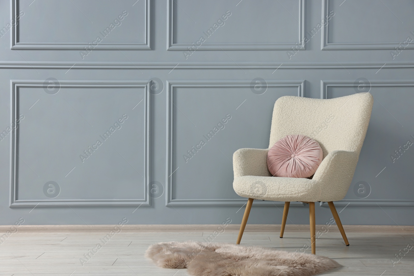 Photo of Stylish armchair with pillow and rug near light grey wall indoors. Space for text