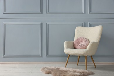 Photo of Stylish armchair with pillow and rug near light grey wall indoors. Space for text