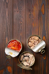 Photo of Tin cans with fish on wooden table, flat lay. Space for text