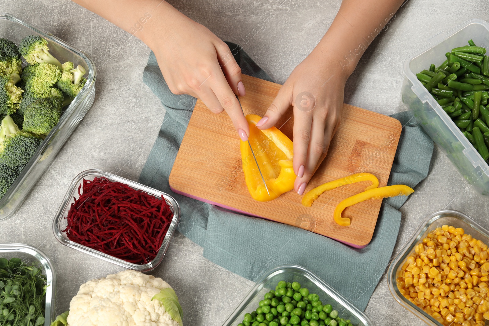 Photo of Woman cutting bell pepper and containers with fresh products on light gray table, top view. Food storage