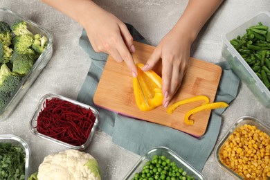 Woman cutting bell pepper and containers with fresh products on light gray table, top view. Food storage