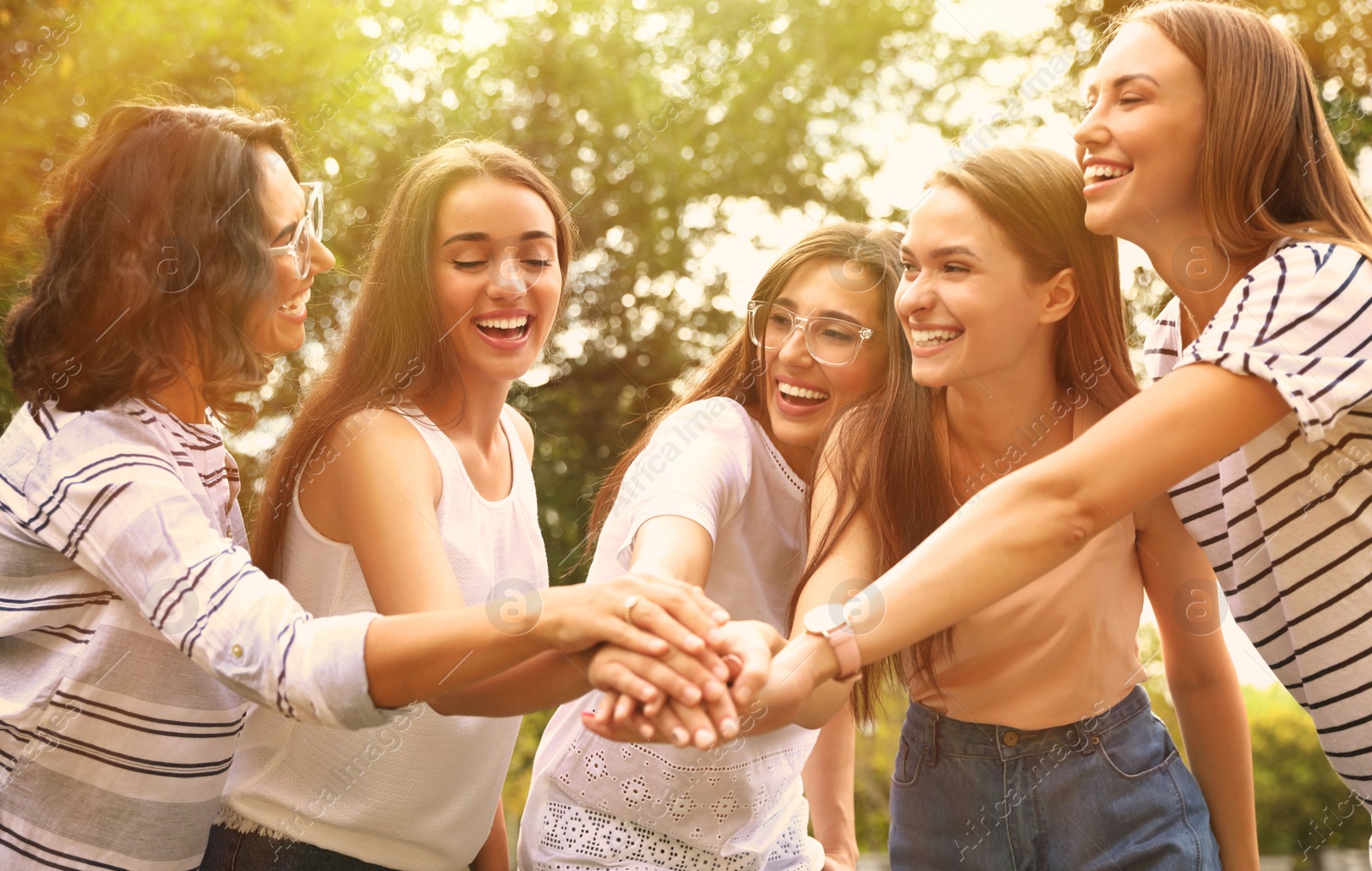 Image of Happy volunteers putting hands together outdoors on sunny day