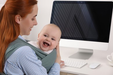 Photo of Mother holding her child in sling (baby carrier) at workplace