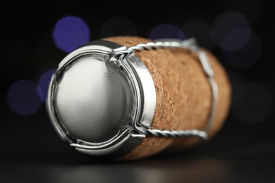 Photo of Sparkling wine cork with muselet cap on table against blurred festive lights, closeup