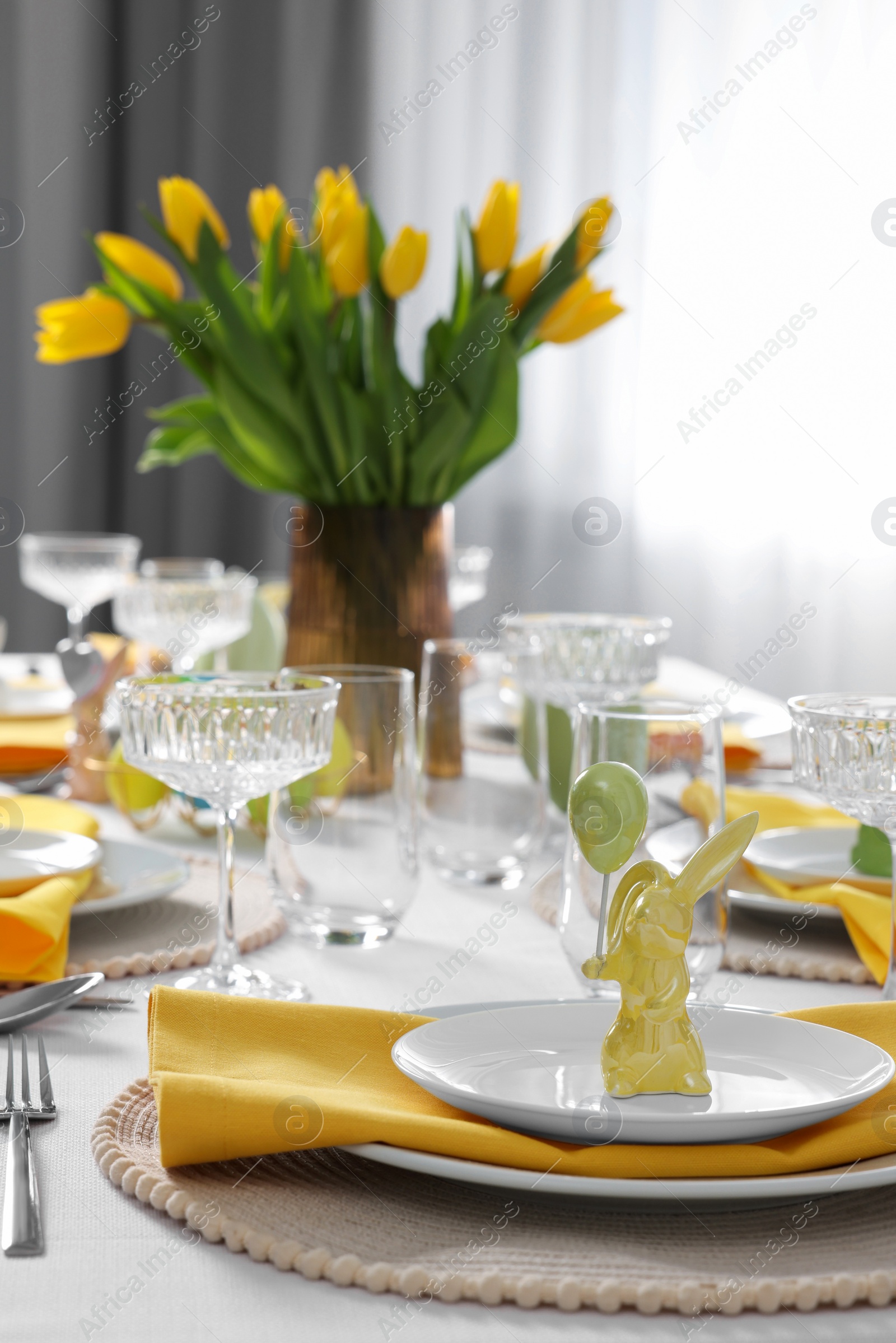 Photo of Festive table setting with glasses, painted eggs and vase of tulips. Easter celebration