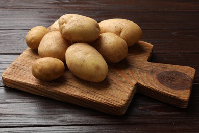 Raw fresh potatoes and cutting board on wooden table