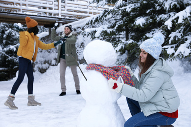 Happy friends making snowman outdoors. Winter vacation