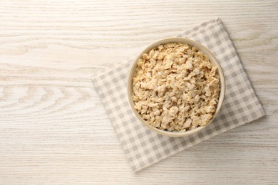 Photo of Tasty boiled oatmeal in bowl on light wooden table, top view. Space for text