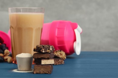 Different energy bars, protein cocktail and powder on blue wooden table. Space for text