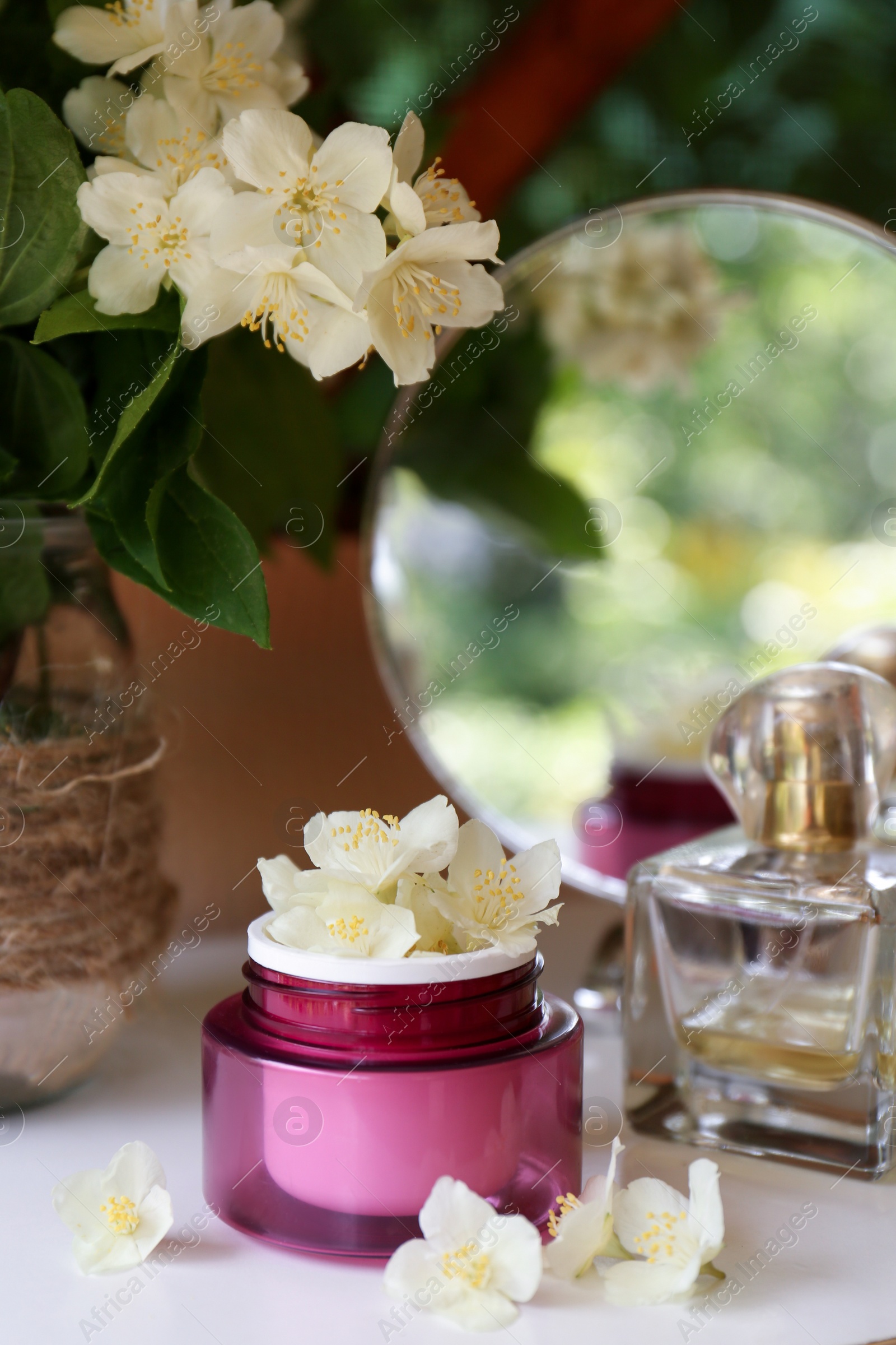 Photo of Jar of cream with beautiful jasmine flowers, perfume and mirror on white table