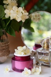Jar of cream with beautiful jasmine flowers, perfume and mirror on white table